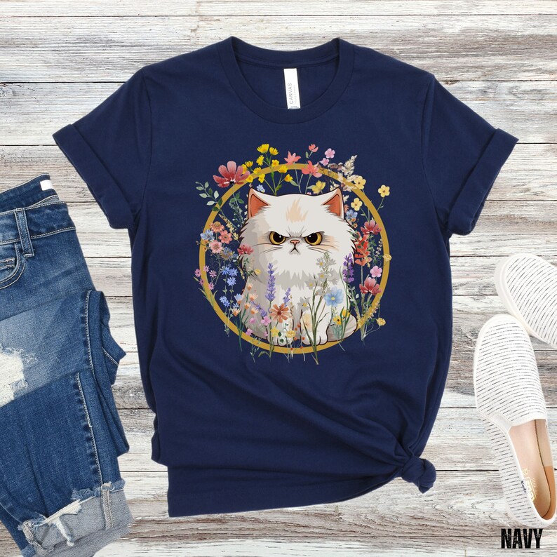 May include: A navy blue t-shirt with a white cat surrounded by colorful flowers in a gold circle. The cat has an angry expression.