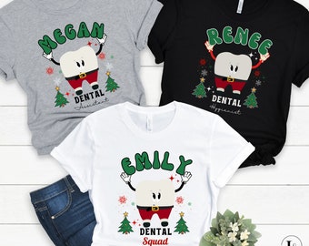 May include: Three t-shirts with dental-themed designs. Each shirt features a cartoon tooth character in a Santa Claus outfit, with names like "Megan," "Renee," and "Emily" above. The shirts are gray, black, and white, with "Dental Assistant," "Dental Hygienist," and "Dental Squad" below.