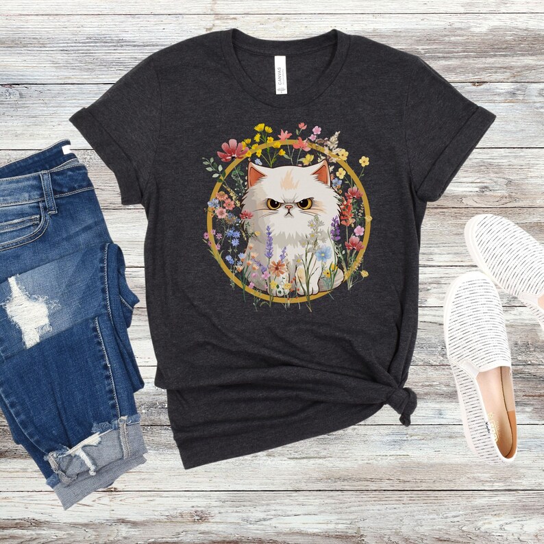 May include: A dark gray t-shirt with a white cat surrounded by colorful flowers in a gold circle. The cat has a grumpy expression.