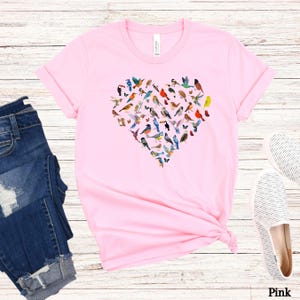 May include: Pink t-shirt featuring a heart-shaped design made up of colourful birds. The shirt is made from a soft, comfortable material and has a relaxed fit.