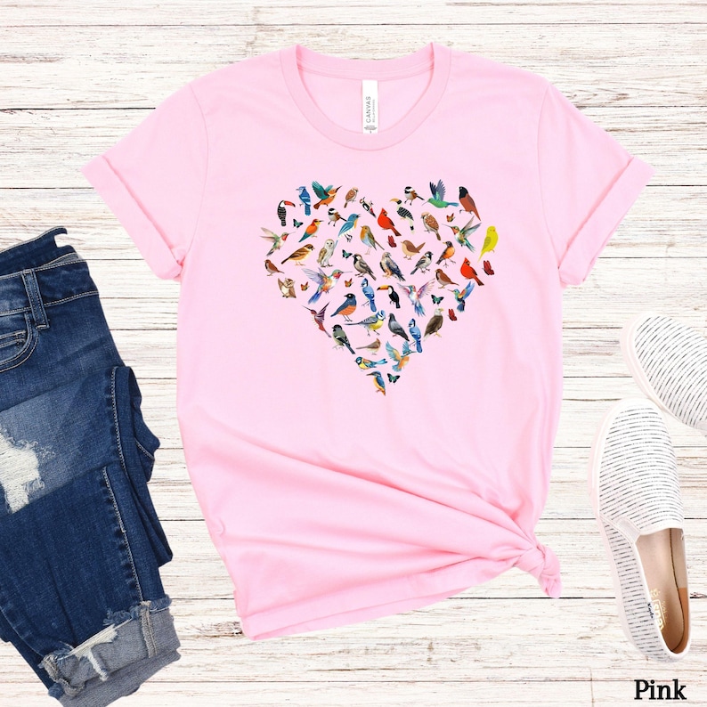 May include: Pink t-shirt featuring a heart-shaped design made up of colourful birds. The shirt is made from a soft, comfortable material and has a relaxed fit.