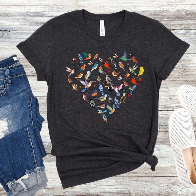 May include: A dark grey t-shirt featuring a heart-shaped design made up of colourful birds. The birds are arranged in a heart shape and are all different colours and sizes.