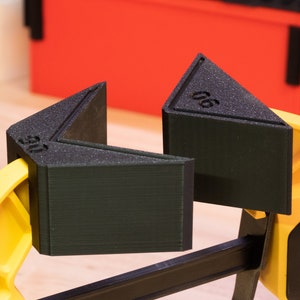 May include: A yellow and black clamp with two black triangular corner clamps. The corner clamps are labeled "06" and "05".