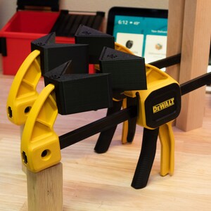 May include: A yellow and black clamp with a black DEWALT logo is holding together three black 3D printed corner braces.