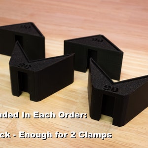 May include: Four black plastic corner clamps, each marked with "90", are arranged on a wooden surface. The text "Included In Each Order: 2 Pack - Enough for 2 Clamps" is visible below the clamps.