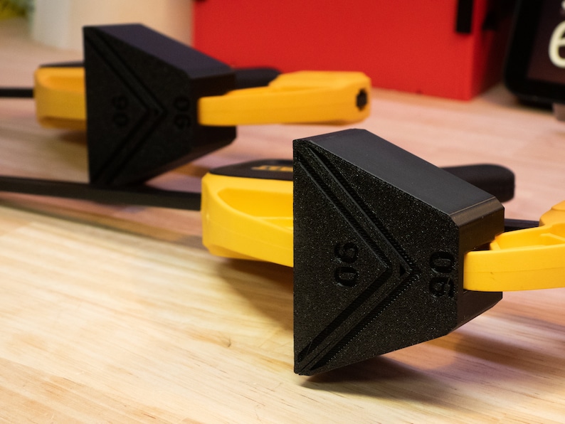 May include: Two black and yellow woodworking clamps with a triangular shape and the number "90" printed on the side.
