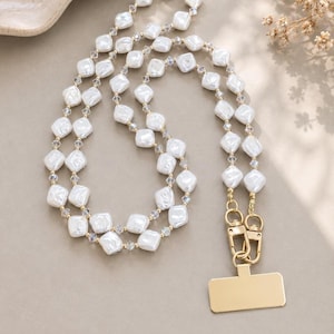 May include: A phone lanyard featuring a double strand of white, diamond-shaped faux pearl beads interspersed with small, clear, faceted crystal spacers. The lanyard includes gold-toned metal lobster clasps attached to a rectangular gold-toned phone tab.