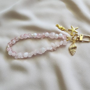 以下が含まれることがあります： ピンクと白のビーズキーホルダー。ゴールドの貝殻、ヒトデ、タツノオトシゴのチャーム付き。