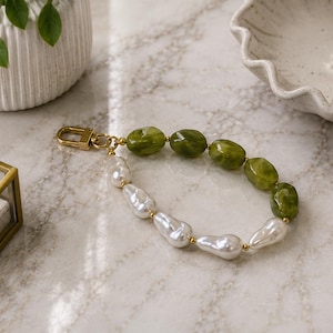May include: A keychain featuring a gold-toned lobster clasp attached to a strand of alternating olive green marbled oval beads and white irregular-shaped faux pearls, connected by small gold-toned metal spacers in a continuous circular loop.