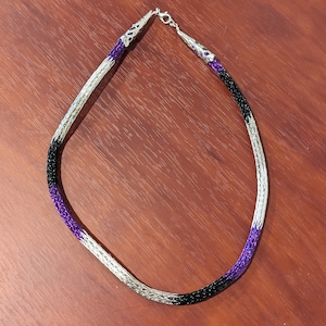 May include: A silver, black, and purple beaded necklace with a silver clasp.