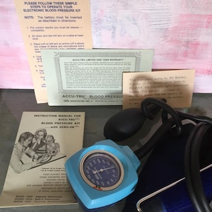 Puede incluir: Un kit electrónico de presión arterial Accu-Tru, con un medidor azul claro, tubos negros y manuales de instrucciones. El kit incluye una garantía de un año e instrucciones de uso. El medidor muestra las mediciones.