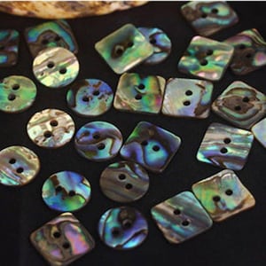 May include: A collection of iridescent buttons in various shapes, including round and square, with two or four holes. The buttons display a range of colors, such as green, blue, and purple, and are likely made from mother-of-pearl or a similar material.