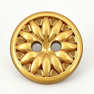 Peut inclure: Un bouton rond en métal doré présentant un motif floral en relief avec des pétales rayonnant depuis le centre. Le bouton possède une surface lisse et réfléchissante, ainsi que deux trous circulaires situés au milieu pour la fixation.