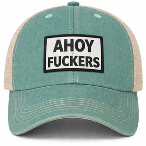 May include: A teal-colored baseball cap with a mesh back and a rectangular patch on the front. The patch features a white background with a black border and the text AHOY FUCKERS printed in bold black capital letters across two lines.