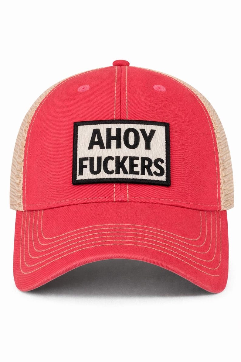 May include: A bright red baseball cap with a tan mesh back and a rectangular patch on the front. The patch is white with a black border and features the black text AHOY FUCKERS in a bold, sans-serif font. The cap has matching red stitching.