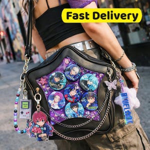 May include: Black star-shaped ita bag with a clear front, filled with character pins and purple accents. The bag has a chain strap and various charms, including a butterfly and a handheld game console.