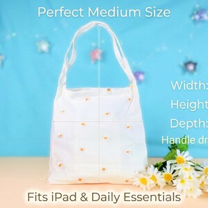 May include: White tote bag with daisy embroidery. The bag is 11 inches wide, 12 inches high, and 5.8 inches deep, with a 9-inch handle drop. The text on the image says "Perfect Medium Size" and "Fits iPad & Daily Essentials."