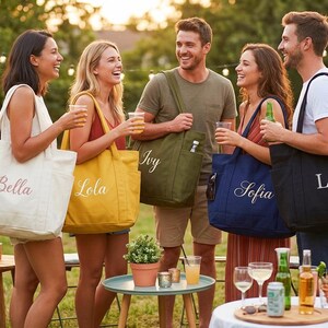 May include: A group of people holding personalized tote bags in various colors, including cream, yellow, olive green, navy blue, and black. Each bag has a name embroidered on it in a cursive font. The scene is outdoors with a blurred background.