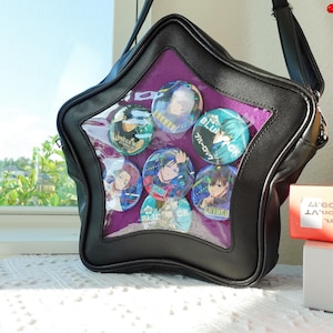 May include: Black star-shaped crossbody bag with a clear front panel displaying several colorful anime-style character buttons. The bag has a purple interior and a black strap. The buttons feature various characters in vibrant colors.