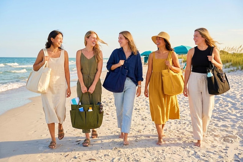 May include: Five people walking on a sandy beach, each carrying a tote bag. The bags are in various colors, including cream, olive green, navy blue, mustard yellow, and black. They are wearing casual summer clothing, including dresses, tops, and pants.