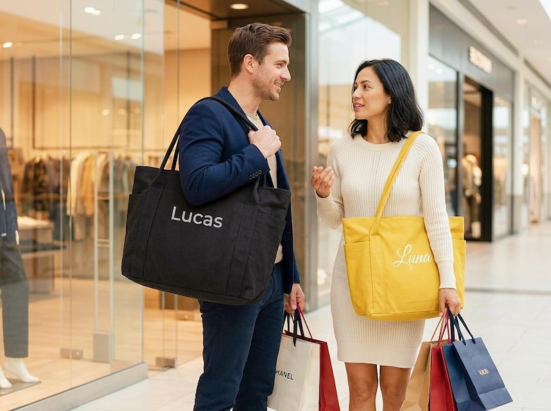 May include: A man and woman are in a shopping mall, each carrying a large tote bag. The man's bag is black with "Lucas" in white. The woman's bag is yellow with "Luna" in white. Both have additional shopping bags.