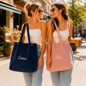 May include: Two corduroy tote bags, one navy blue with "Emma" embroidered in white, and a pink one with "Lily" embroidered. Both bags have long straps and are carried by people in a sunny outdoor setting.