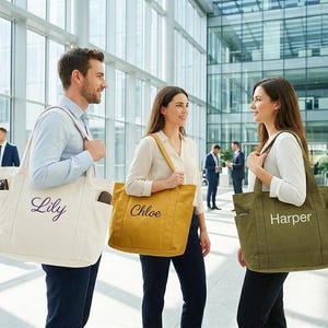 May include: Three people in a modern office setting each carry a personalized tote bag. The bags are in cream, mustard yellow, and olive green, with the names "Lily", "Chloe", and "Harper" embroidered on them. The bags have pockets and are carried over the shoulder.