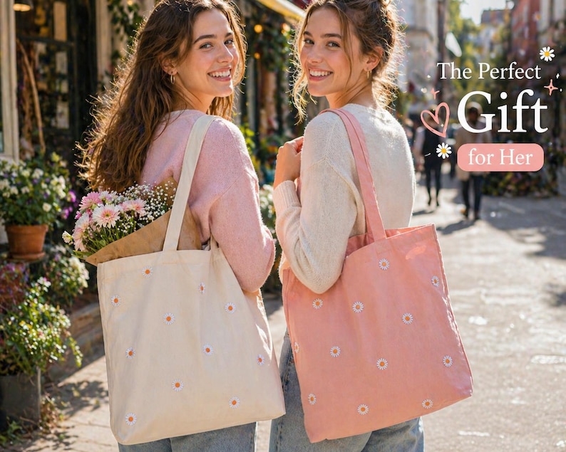 May include: Two women holding tote bags with daisy embroidery. One bag is cream-colored, the other is pink. The bags have long straps and are filled with flowers. The text "The Perfect Gift for Her" is visible.