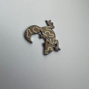 Peut inclure: Une épingle en émail marron et crème représentant un gecko stylisé avec un motif en spirale.