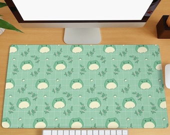 May include: A green and white desk mat with a repeating pattern of frogs and leaves. The mat is on a wooden surface with a computer monitor, keyboard, and mouse.