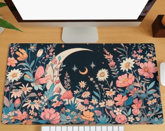 May include: A dark blue desk mat with a crescent moon and floral design. The flowers are pink, white, and yellow. The moon is white and has a star inside it. The mat is surrounded by a computer monitor, keyboard, and mouse.