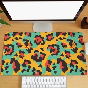 Puede incluir: Una alfombrilla de escritorio de estampado de leopardo amarillo, verde, negro y rojo con un teclado blanco y un ratón blanco sobre una superficie de madera.