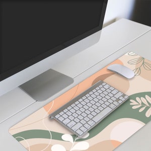 May include: A white keyboard and mouse are on a desk mat with an abstract design featuring peach, brown, and green colors. The design includes leaves and wavy lines.