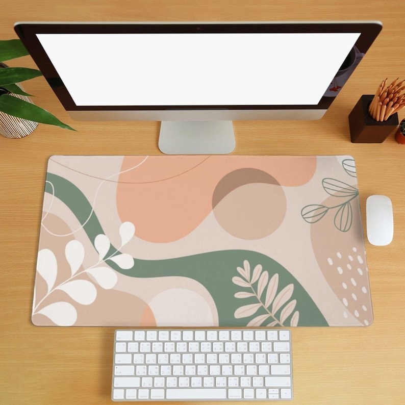 May include: A desk mat with an abstract design featuring peach, brown, and green shapes with white leaf outlines. The mat is on a wooden desk with a computer monitor, keyboard, and mouse.