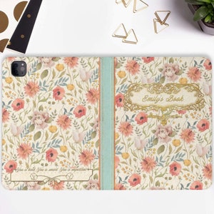 Peut inclure: Une coque de téléphone à motif floral avec un cadre doré et le texte "Emily's Book" au dos. La coque a un ruban bleu clair au centre.