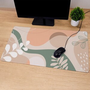 May include: A beige and green abstract design mouse pad with a black computer mouse on top. The mouse pad features white and green leaves and abstract shapes.