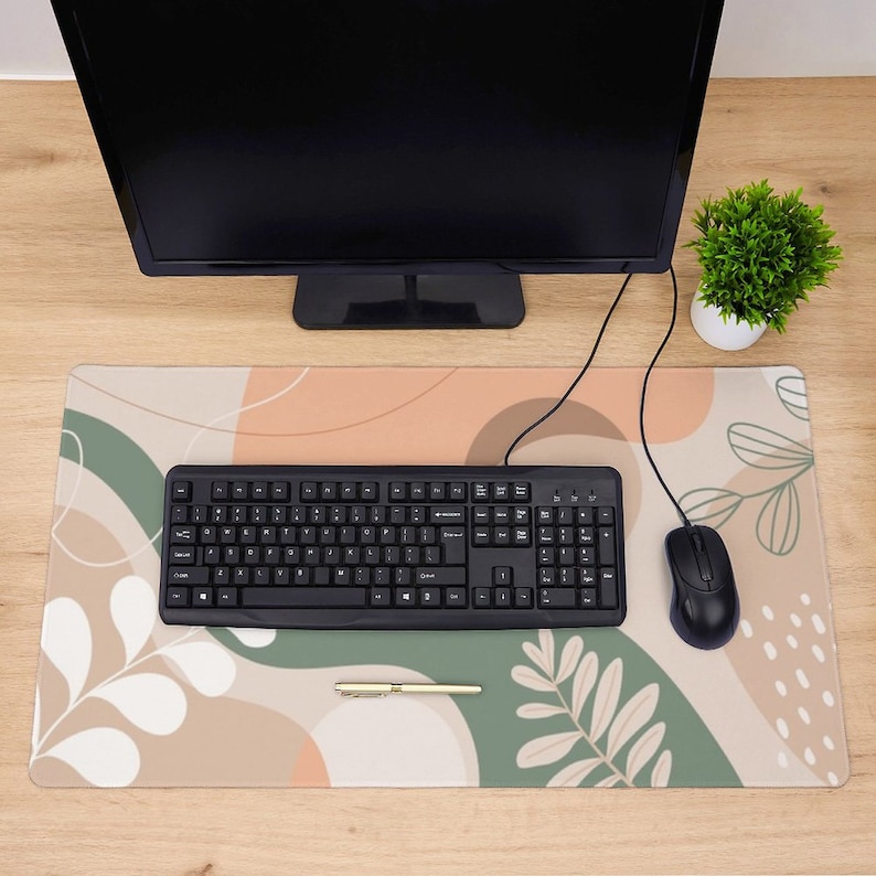 May include: A beige and green desk mat with an abstract design featuring leaves and swirls. A black keyboard and a black computer mouse are on the mat.