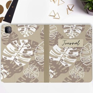May include: A beige journal cover with a white monstera leaf pattern. The cover has a label that says "Journal".