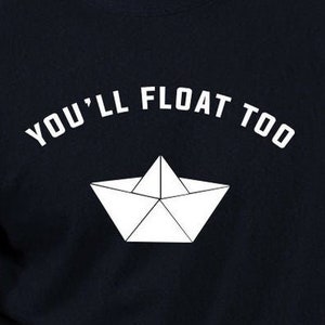 Könnte beinhalten: Ein schwarzes T-Shirt mit weißem Text, der "You'll Float Too" lautet, und einer weißen Papierbootgrafik.