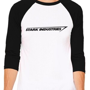 Puede incluir: Una camiseta de b&eacute;isbol blanca y negra con un logotipo negro que dice "Stark Industries" con una l&iacute;nea diagonal.