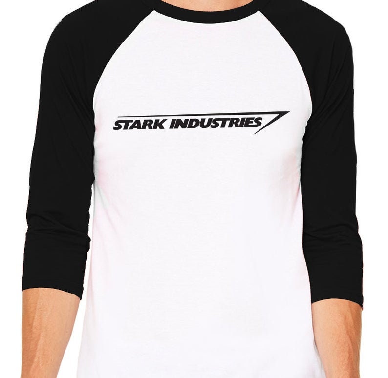 Puede incluir: Una camiseta de b&eacute;isbol blanca y negra con un logotipo negro que dice "Stark Industries" con una l&iacute;nea diagonal.