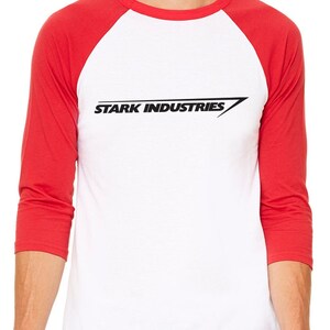 Puede incluir: Una camiseta de b&eacute;isbol blanca con mangas rojas que muestra el texto "STARK INDUSTRIES" en negro con una l&iacute;nea diagonal.