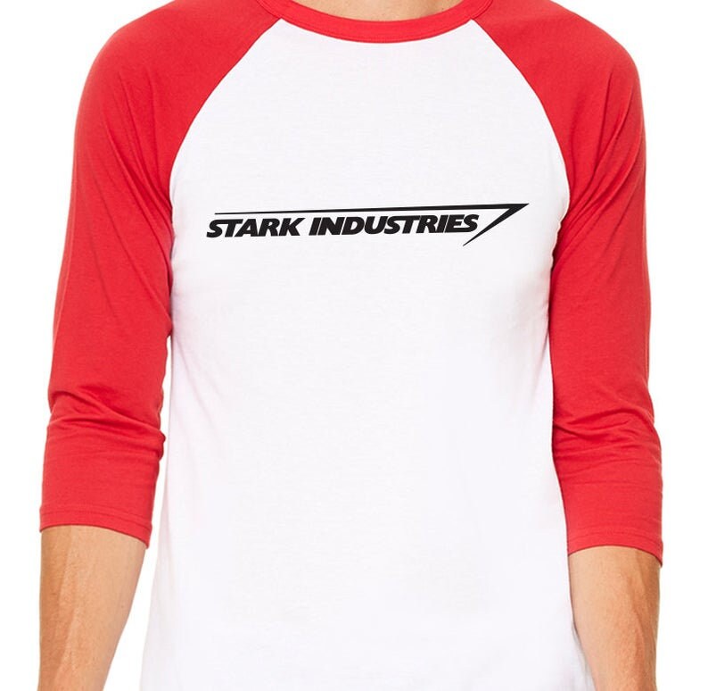 Puede incluir: Una camiseta de b&eacute;isbol blanca con mangas rojas que muestra el texto "STARK INDUSTRIES" en negro con una l&iacute;nea diagonal.