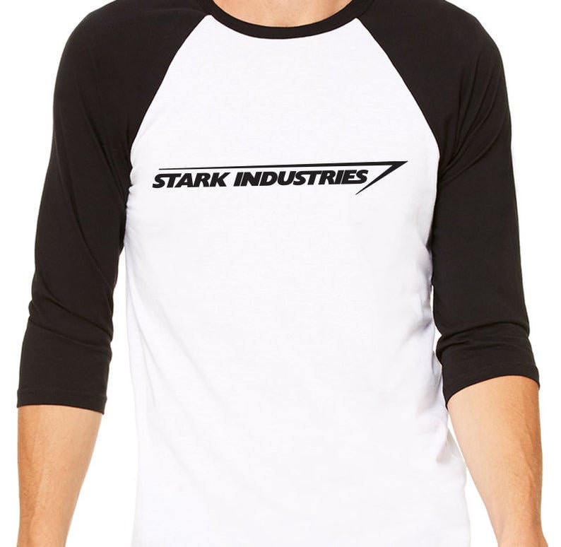 Puede incluir: Una camiseta de b&eacute;isbol blanca y negra con un logotipo negro que dice "STARK INDUSTRIES" en una fuente inclinada.