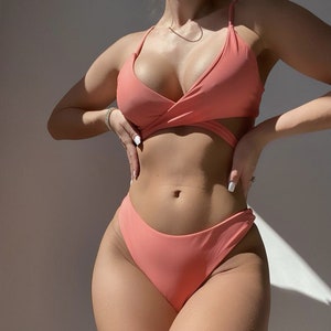 May include: A coral pink bikini top with a wrap style and a matching high-cut bikini bottom.