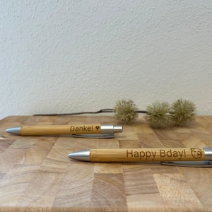 Puede incluir: Dos bol&iacute;grafos de bamb&uacute; con detalles plateados. El bol&iacute;grafo superior tiene el texto "Danke!" con un s&iacute;mbolo de coraz&oacute;n. El bol&iacute;grafo inferior tiene el texto "Happy Bday!" con un peque&ntilde;o s&iacute;mbolo de huella de pata.