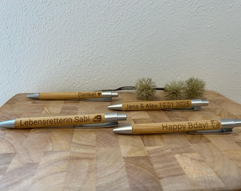 Puede incluir: Cuatro bolígrafos de madera con detalles plateados y mensajes personalizados. Los mensajes incluyen "Danke!" con un corazón, "Lebensretterin Sabi" con un pequeño icono de coche, "Jana & Alex 19.01.2025" y "Happy Bday!" con un pequeño icono de perro.