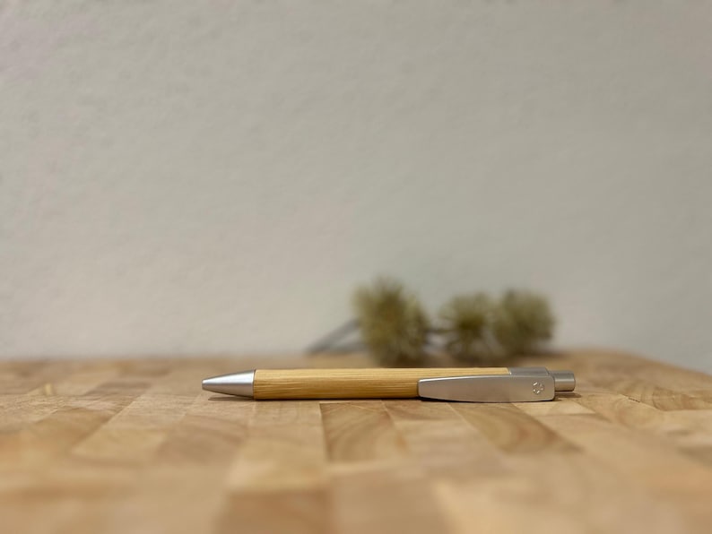 Puede incluir: Un bol&iacute;grafo de madera con un clip plateado y una punta plateada. El bol&iacute;grafo est&aacute; sobre una superficie de madera.