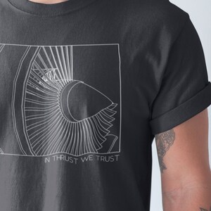 May include: A dark gray t-shirt with a white outline of a jet engine and the text "In Thrust We Trust".