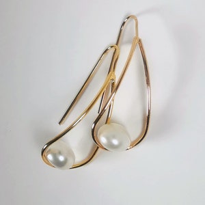 May include: A pair of gold earrings with a simple, curved design. Each earring features a single white pearl.